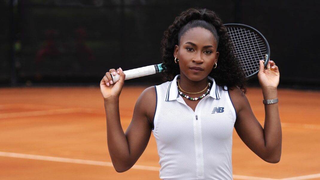 Tennis player Coco Gauff in white New Balance athletic top and visor at a major tournament, representing her prominent corporate endorsement portfolio.